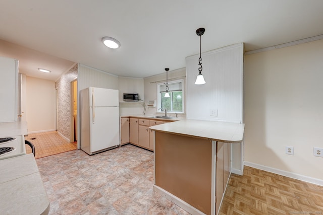 kitchen featuring freestanding refrigerator, stainless steel microwave, a peninsula, light countertops, and decorative light fixtures
