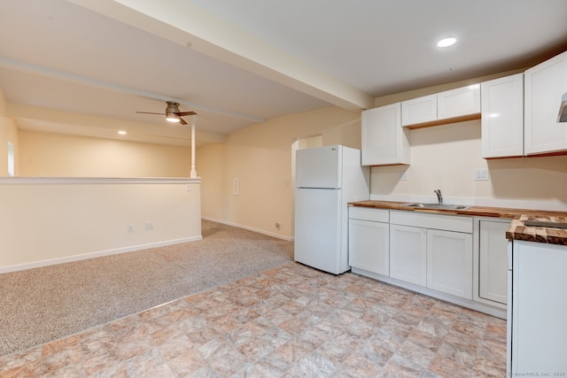 kitchen featuring freestanding refrigerator, white cabinetry, a ceiling fan, a sink, and light carpet