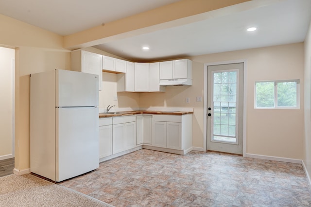 kitchen featuring freestanding refrigerator, under cabinet range hood, white cabinetry, baseboards, and recessed lighting