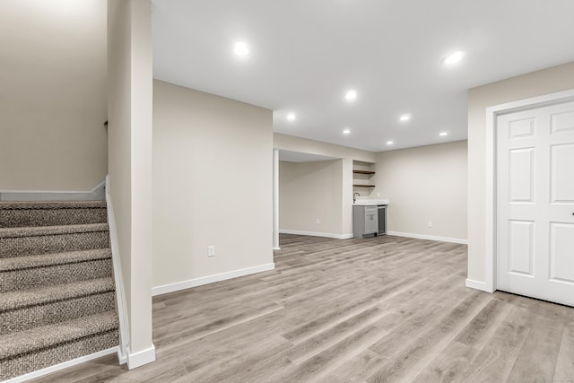 finished basement featuring stairway, light wood-type flooring, baseboards, recessed lighting, and bar