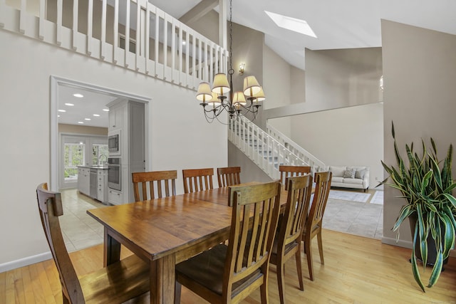 dining space featuring a skylight, high vaulted ceiling, light wood-style flooring, a chandelier, and stairway