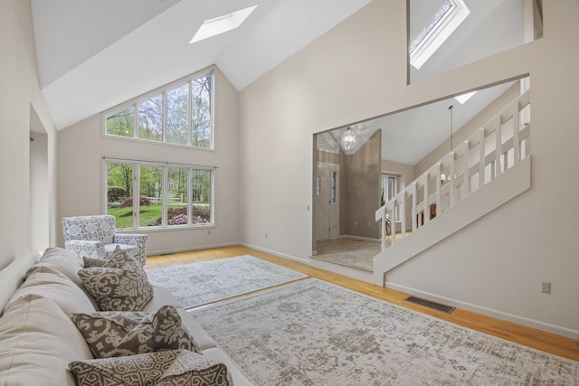 living area featuring a skylight, high vaulted ceiling, wood finished floors, baseboards, and stairs