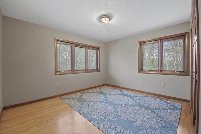 unfurnished room featuring plenty of natural light, baseboards, light wood-style flooring, and a textured ceiling