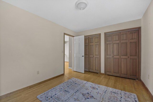 bedroom with multiple closets, light wood-style flooring, and baseboards
