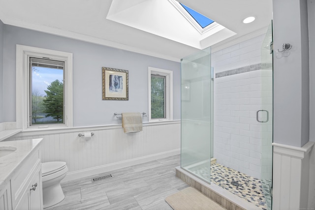 bathroom with a skylight, a stall shower, a wainscoted wall, toilet, and vanity