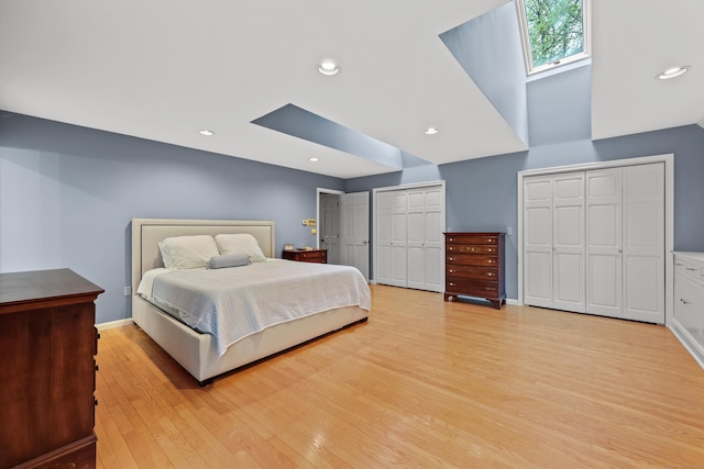 bedroom with a skylight, light wood-type flooring, multiple closets, recessed lighting, and baseboards