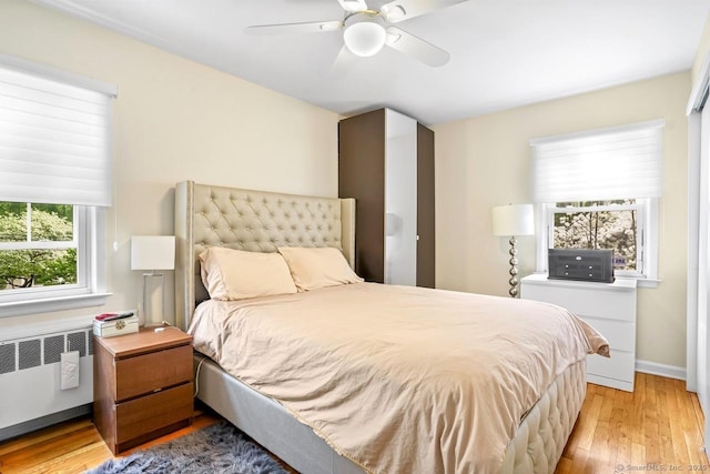 bedroom featuring radiator heating unit, light wood finished floors, ceiling fan, and baseboards