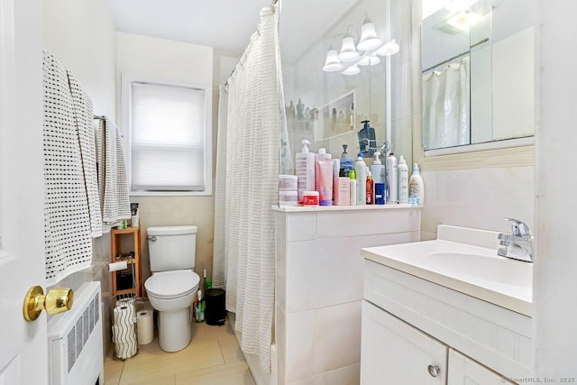bathroom with radiator, toilet, tile patterned floors, vanity, and tile walls