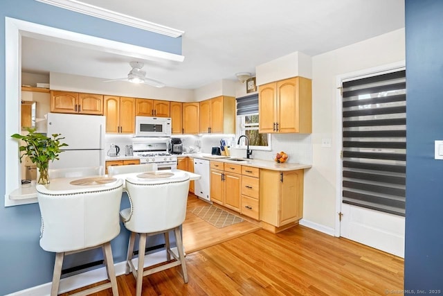 kitchen with white appliances, light countertops, light wood finished floors, a sink, and a breakfast bar