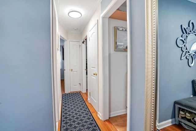 hallway featuring light wood-style floors, ornamental molding, and baseboards