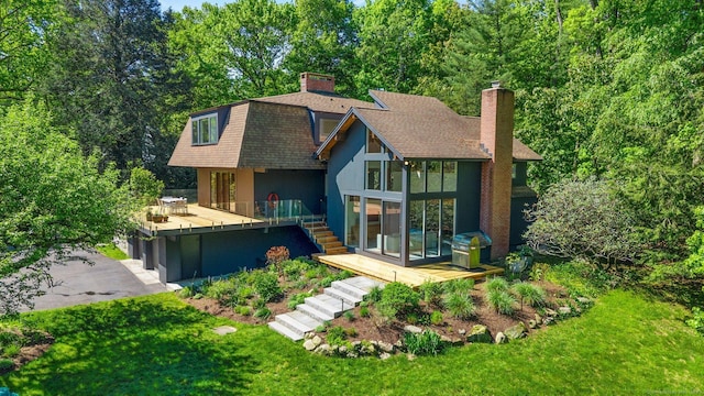 back of property with a shingled roof, a chimney, a lawn, stairway, and stucco siding