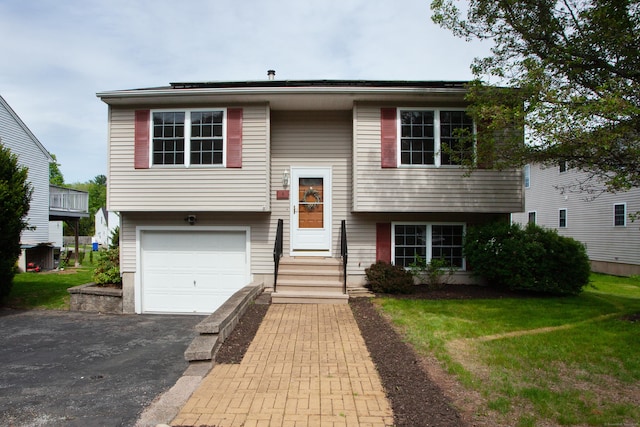 bi-level home featuring asphalt driveway, an attached garage, entry steps, and a front yard