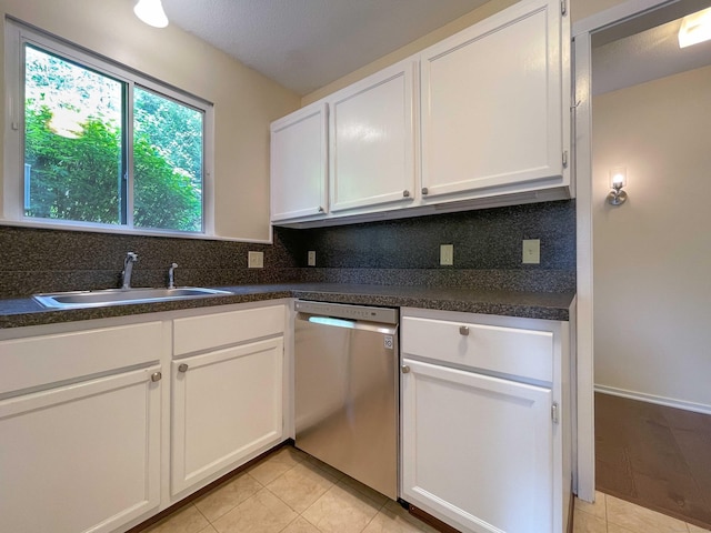 kitchen featuring stainless steel dishwasher, a sink, tasteful backsplash, white cabinetry, and light tile patterned floors