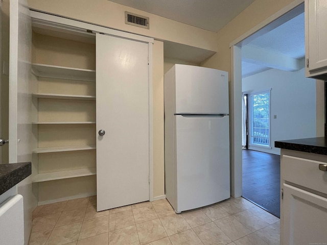 kitchen with freestanding refrigerator, dark countertops, and white cabinets
