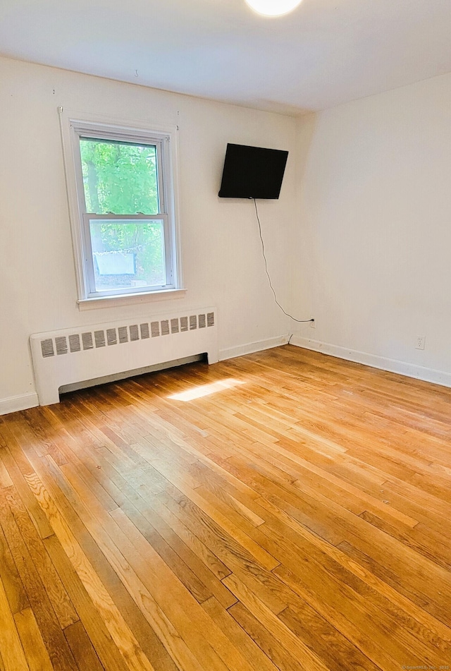 unfurnished room with radiator, light wood-style flooring, and baseboards
