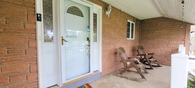 doorway to property with covered porch and brick siding