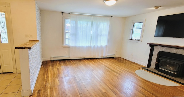 unfurnished living room featuring a wood stove, a baseboard radiator, baseboards, and wood finished floors