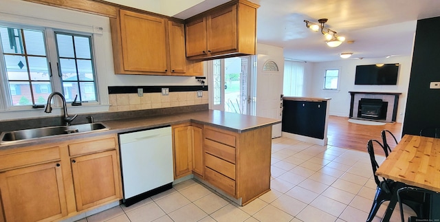 kitchen featuring dishwasher, a sink, a peninsula, light tile patterned floors, and a tiled fireplace
