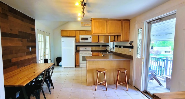 kitchen featuring white appliances, light tile patterned floors, a peninsula, a sink, and brown cabinetry