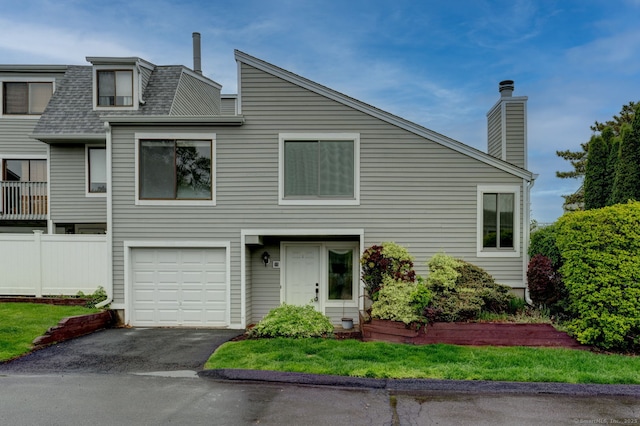 view of front facade with a shingled roof, driveway, a chimney, a garage, and fence