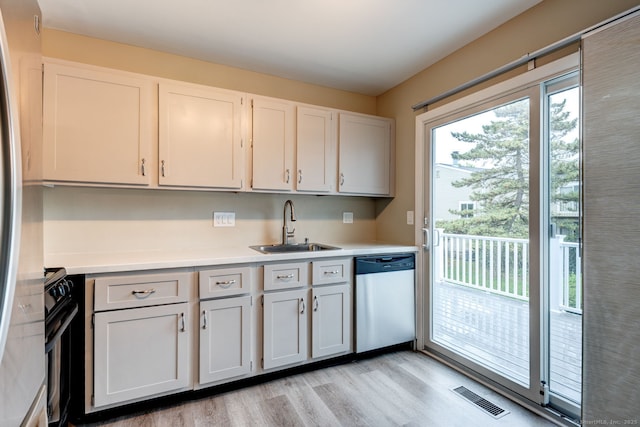 kitchen featuring appliances with stainless steel finishes, a sink, light wood-type flooring, light countertops, and white cabinets