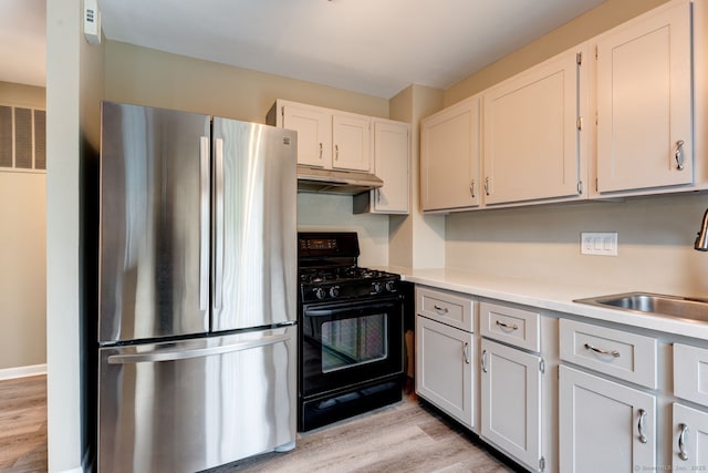 kitchen featuring freestanding refrigerator, black range with gas cooktop, a sink, under cabinet range hood, and light wood-type flooring