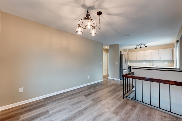 kitchen with freestanding refrigerator, light wood-style floors, white cabinets, baseboards, and a chandelier