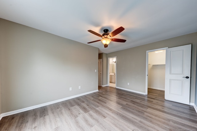 unfurnished bedroom featuring a walk in closet, wood finished floors, baseboards, a closet, and ensuite bathroom