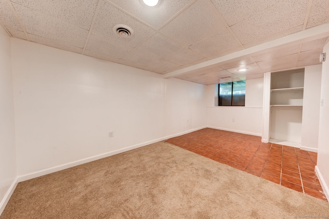 carpeted spare room featuring baseboards, tile patterned flooring, and a paneled ceiling