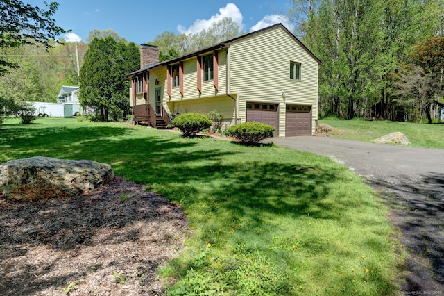 view of front of house featuring an attached garage, a chimney, asphalt driveway, and a front lawn
