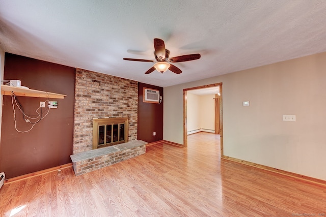 unfurnished living room with a wall mounted AC, a ceiling fan, wood finished floors, and a fireplace