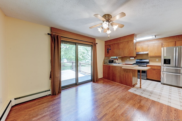 kitchen with appliances with stainless steel finishes, light countertops, a peninsula, under cabinet range hood, and a sink