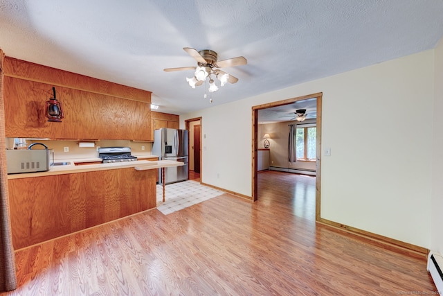 kitchen with stainless steel appliances, brown cabinets, light wood-type flooring, and a ceiling fan