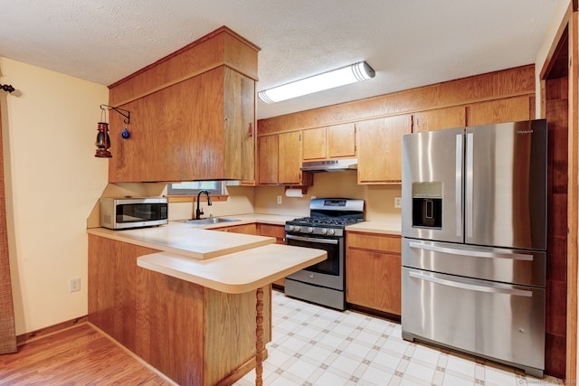 kitchen featuring stainless steel appliances, a sink, under cabinet range hood, a peninsula, and light countertops