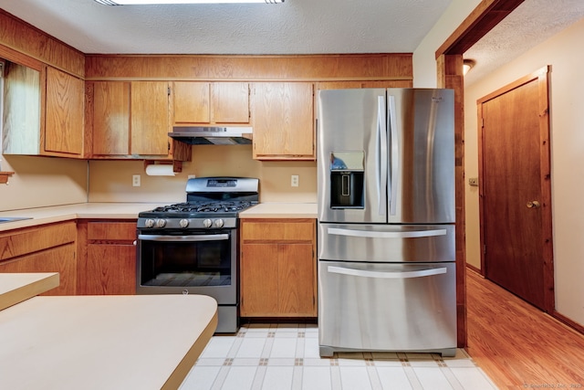 kitchen featuring stainless steel appliances, under cabinet range hood, light countertops, light flooring, and a textured ceiling