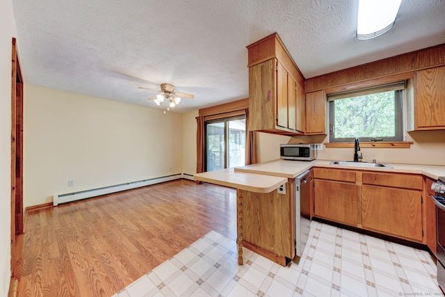 kitchen with appliances with stainless steel finishes, a sink, a baseboard heating unit, plenty of natural light, and a textured ceiling
