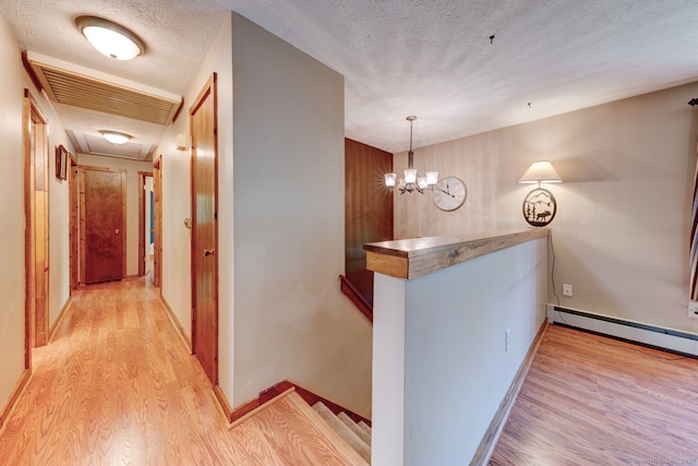 hallway with an upstairs landing, light wood-type flooring, a textured ceiling, baseboards, and a chandelier
