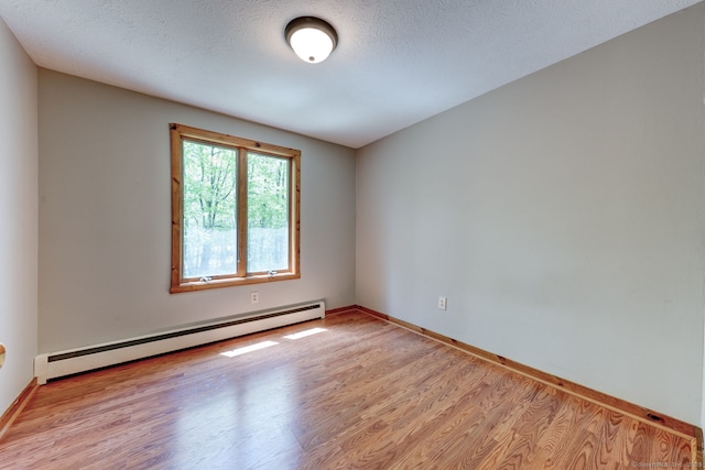 spare room featuring baseboard heating, light wood-style flooring, baseboards, and a textured ceiling