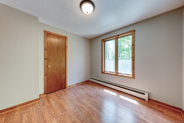 empty room with a baseboard radiator, light wood-type flooring, baseboards, and a textured ceiling