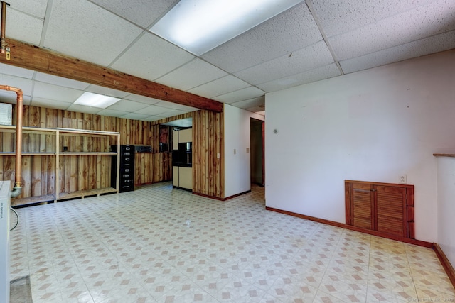 finished basement featuring a drop ceiling, baseboards, and wood walls