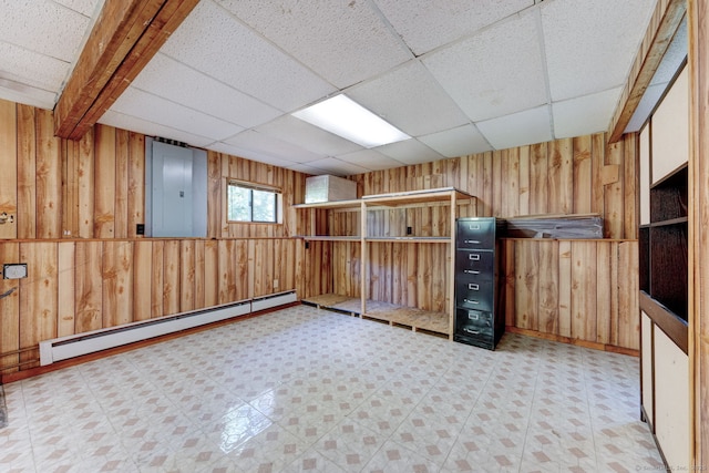 unfurnished room featuring baseboard heating, wooden walls, electric panel, a drop ceiling, and light floors