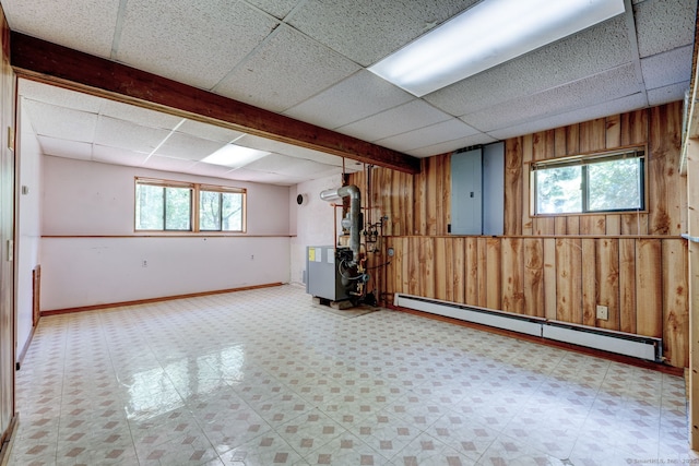 below grade area with baseboard heating, wooden walls, a drop ceiling, tile patterned floors, and electric panel