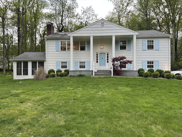 view of front facade with a chimney, a front lawn, a sunroom, and covered porch