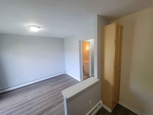 spare room with a baseboard heating unit, wood finished floors, baseboards, and baseboard heating