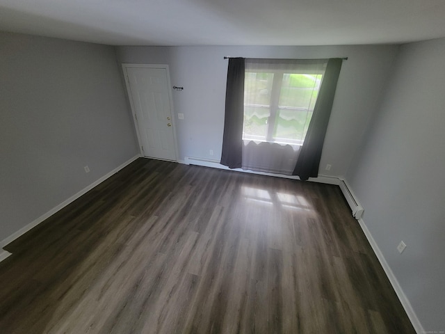 empty room with dark wood finished floors, a baseboard heating unit, and baseboards