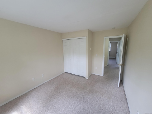 unfurnished bedroom featuring light carpet, baseboards, a closet, and a baseboard heating unit