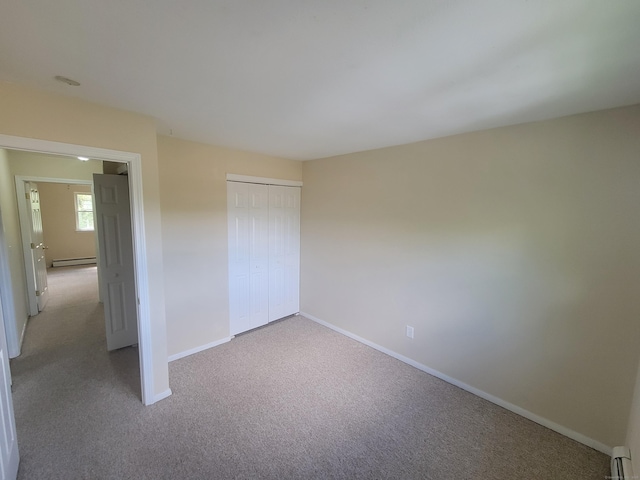 unfurnished bedroom featuring baseboard heating, carpet flooring, baseboards, and a closet