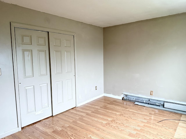 unfurnished bedroom with light wood finished floors, a closet, a baseboard heating unit, and baseboards