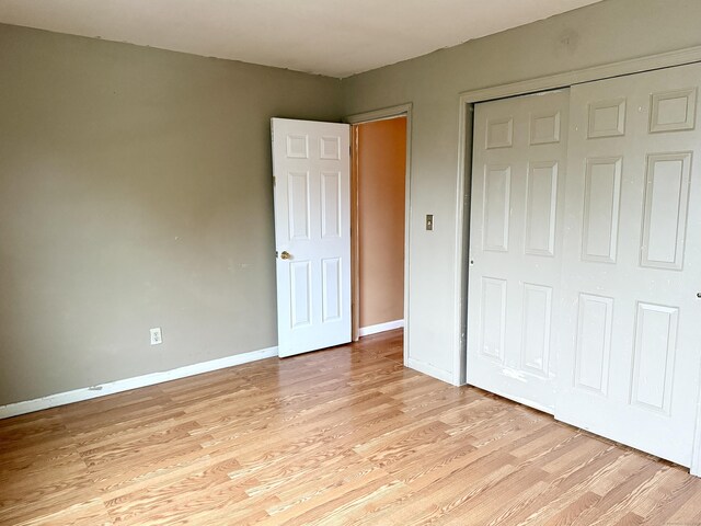 unfurnished bedroom with light wood-style flooring, a closet, and baseboards
