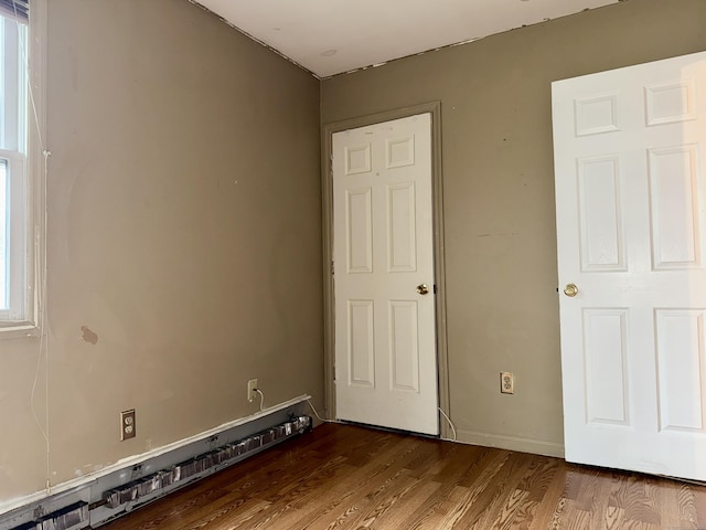 unfurnished bedroom with dark wood-type flooring and a baseboard heating unit